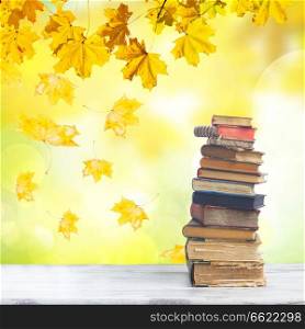 stack of books on white wooden desktop, fall tree leaves in background. set of books