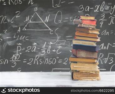 stack of books on white wooden table with math formulas on blackboard. set of books