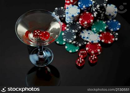 Stack of Casino gambling chips, glass of martini vermouth and red dices isolated on reflective black background.. Stack of Casino gambling chips, glass of martini vermouth and red dices isolated on reflective black background