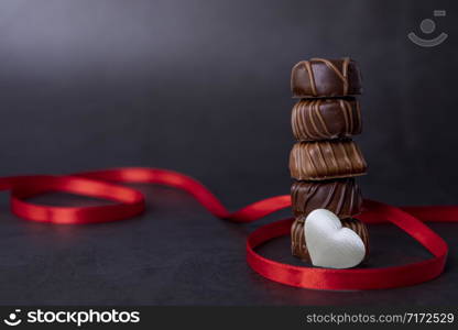 Stack of Chocolate candy and red ribbon on a black background. Focus on chocolates