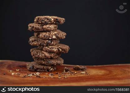 stack of chocolate chip and oakmeal cookies on natural wood texture on black background, selective focus