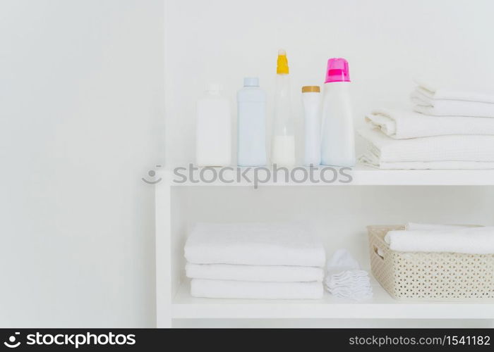 Stack of clean white towels with detergents on console isolated over white background. Fresh laundry and liquid washing in bathroom