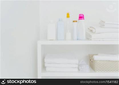 Stack of clean white towels with detergents on console isolated over white background. Fresh laundry and liquid washing in bathroom