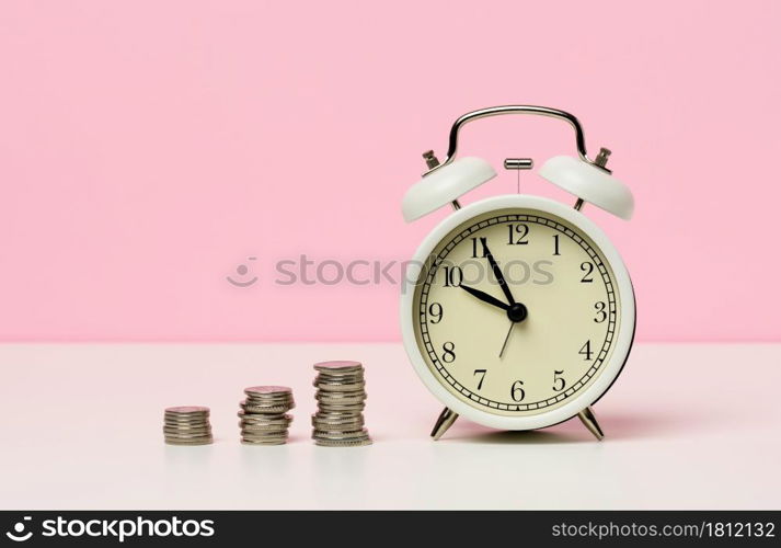 stack of coins round white alarm clock on the table. The concept of time is money, a period of discounts.