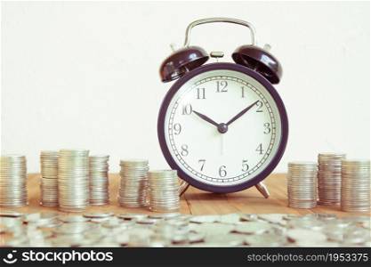 Stack of coins with black fashioned alarm clock for display planning money financial and business accounting concept, time is money concept with clock and coins, time to work at make money, vintage color tone