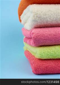 stack of colored cotton terry folded towels on a blue background, close up
