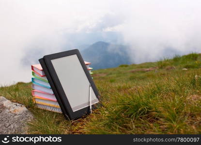 Stack of colorful books and electronic book reader on the grass