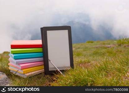 Stack of colorful books and electronic book reader on the grass