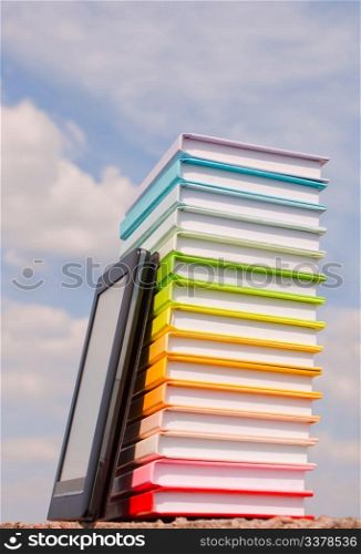 Stack of colorful books and electronic book reader outdoors