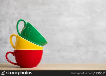 stack of colorful coffee cups on wall background at cafe. Green, yellow and red color ceramic mug on table at home. International coffee day concept