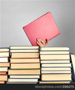 stack of different books on a gray background, hand hold a book in red hardcover