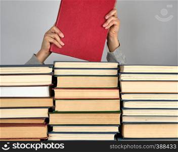 stack of different books on a gray background, hands hold a book in red hardcover
