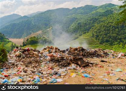 Stack of different types of large garbage dump, plastic bags, and trash burning near paddy rice terraces, agricultural fields of Mu Cang Chai, mountain in Vietnam in environmental pollution concept.