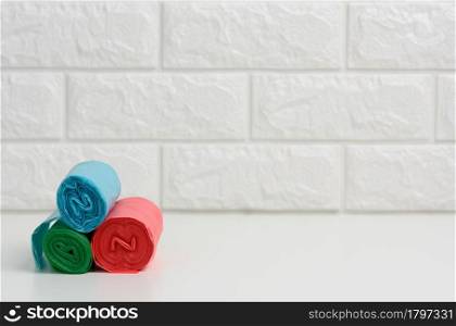 stack of disposable plastic trash can bags on white table, white brick wall background, copy space