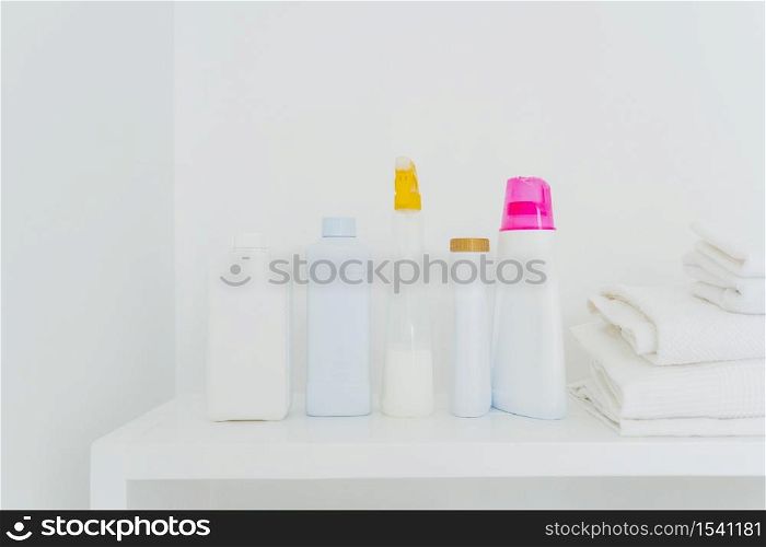 Stack of folded white towels and bottles with detergent against white background. Washing and cleanliness concept. Space for your text