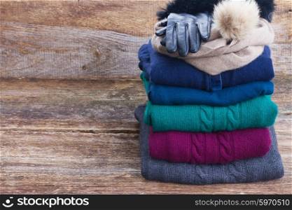 stack of folded woolen gray, green, blue and red clothes on wooden background with copy space