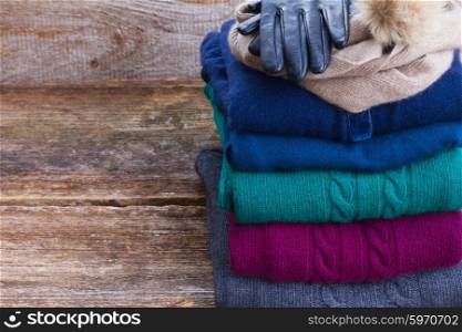 stack of folded woolen gray, green, blue and red clothes on wooden background close up with copy space