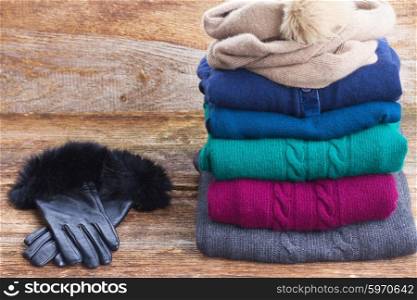 stack of folded woolen gray, green, blue and red clothes with gloves on wooden background