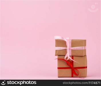 stack of gifts in boxes wrapped in brown kraft paper and tied with silk ribbon on a pink background. Festive concept, copy space