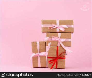 stack of gifts in boxes wrapped in brown kraft paper and tied with silk ribbon on a pink background. Festive concept