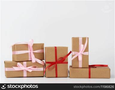 stack of gifts in boxes wrapped in brown kraft paper and tied with silk ribbon on a white background. Festive concept, copy space