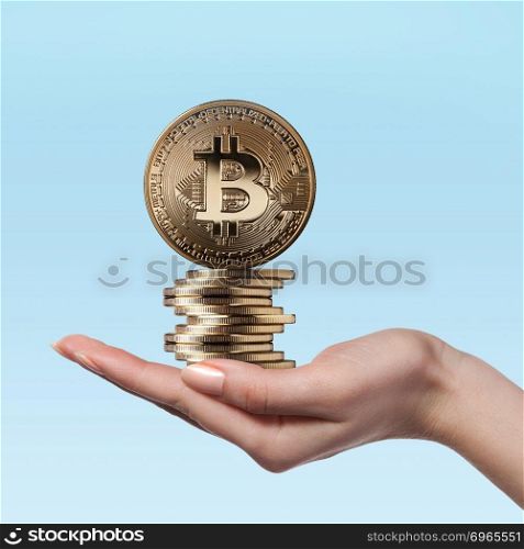 Stack of gold bitcoins in a female hand on a blue background. Virtual money, crypto currency. Female hand holds gold coins bitcoin