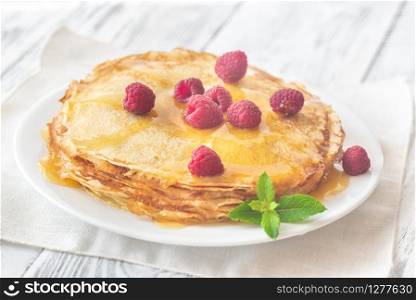 Stack of homemade crepes with fresh raspberries and sweet topping on the white plate