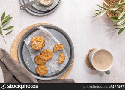 Stack of homemade oatmeal cookies, healthy breakfast cereal oat crackers and mug of milk with coffee on white kitchen countertop. Top view. Flat lay