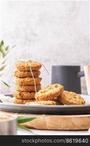 Stack of homemade oatmeal cookies, healthy breakfast cereal oat crackers and mug of milk with coffee on white kitchen countertop