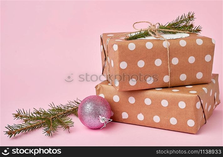 stack of kraft paper wrapped gifts, spruce branch on pink background. Christmas greeting concept
