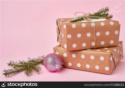stack of kraft paper wrapped gifts, spruce branch on pink background. Christmas greeting concept