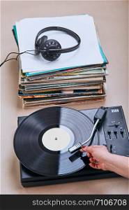 Stack of many black vinyl records, turntable vinyl player and headphones put on the stack. Classic stereo set. Candid people, real moments, authentic situations