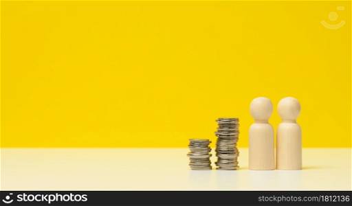 stack of metal coins and wooden figures of men on a white table. Savings and expenses, family budget, subsidies from the state, copy space