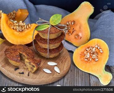 stack of muffins with a pumpkin on a round wooden board and fresh pieces of pumpkin