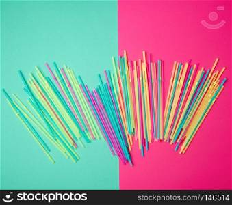 stack of multi-colored plastic tubes for a cocktail on a multi-colored background, concept of environmental pollution by objects that decay in the ground for a long time, top view