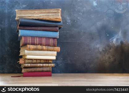 Stack of multicolored books on boockshelf, education, reading, back to school concept, copy space on blackboard. Pile of old books