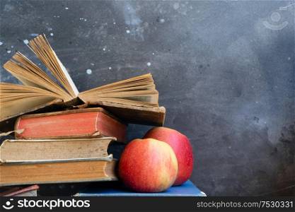 Stack of multicolored books with two apples, education, reading, back to school concept, copy space on blackboard. Pile of old books