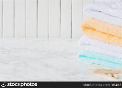 Stack of multicolored fluffy cotton bath towels and wooden clothespins are on the background of marble surface, with copy-space
