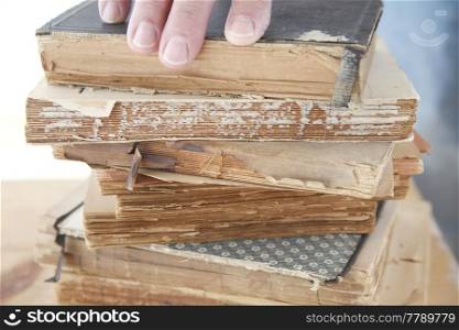 stack of old books with a man&rsquo;s fingers on top