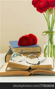 Stack of old books with red ranunculus flowers posy. Old books with rose flower