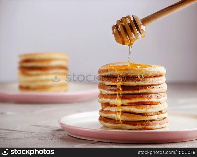 Stack of Pancakes with honey spoon and pouring honey on light back. Stack of Pancakes with honey spoon and pouring honey on light background