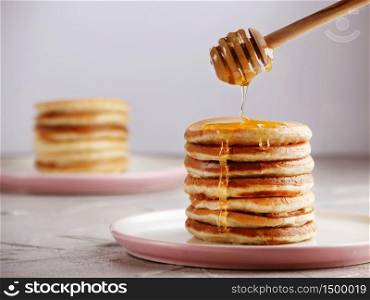 Stack of Pancakes with honey spoon and pouring honey on light back. Stack of Pancakes with honey spoon and pouring honey on light background