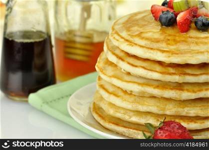 stack of pancakes with maple syrup,honey and berries