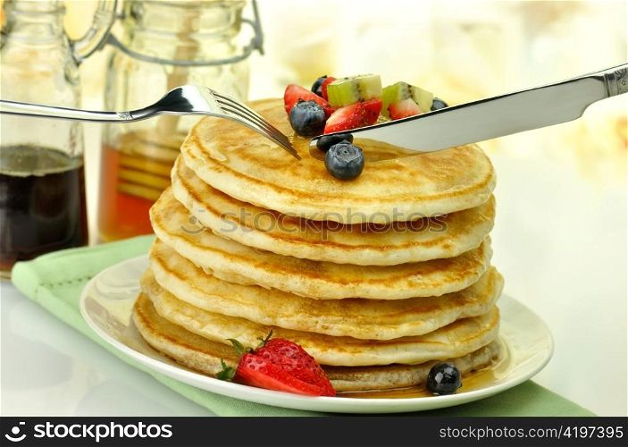 stack of pancakes with maple syrup,honey and berries