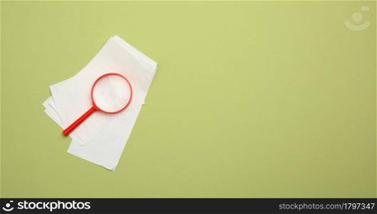 stack of paper sales receipts and red plastic magnifying glass on a green background. The concept of control of expenses and income, budget planning, copy space