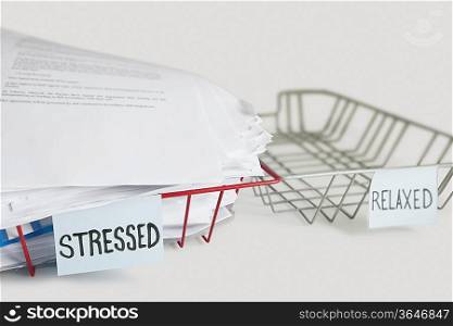 Stack of paperwork in stressed tray with empty relaxed platter over white background