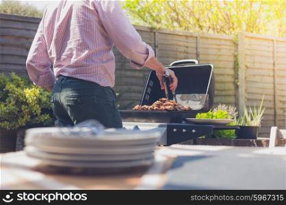 Stack of plates on a table outside in a garden with a man attending to a barbecue in the background