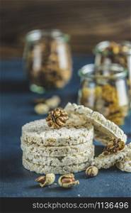 Stack of rice cakes. American puffed rice cakes. Healthy snacks with almonds, raisins, peanuts, pistachios in glass jars on classic blue concrete surface. Close up.