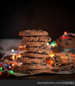 stack of round chocolate cookies, behind the burning lights of a Christmas garland