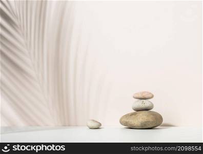 stack of round stones and and the shadow of a palm leaf on a beige background. Scene for demonstration of cosmetic products, advertising